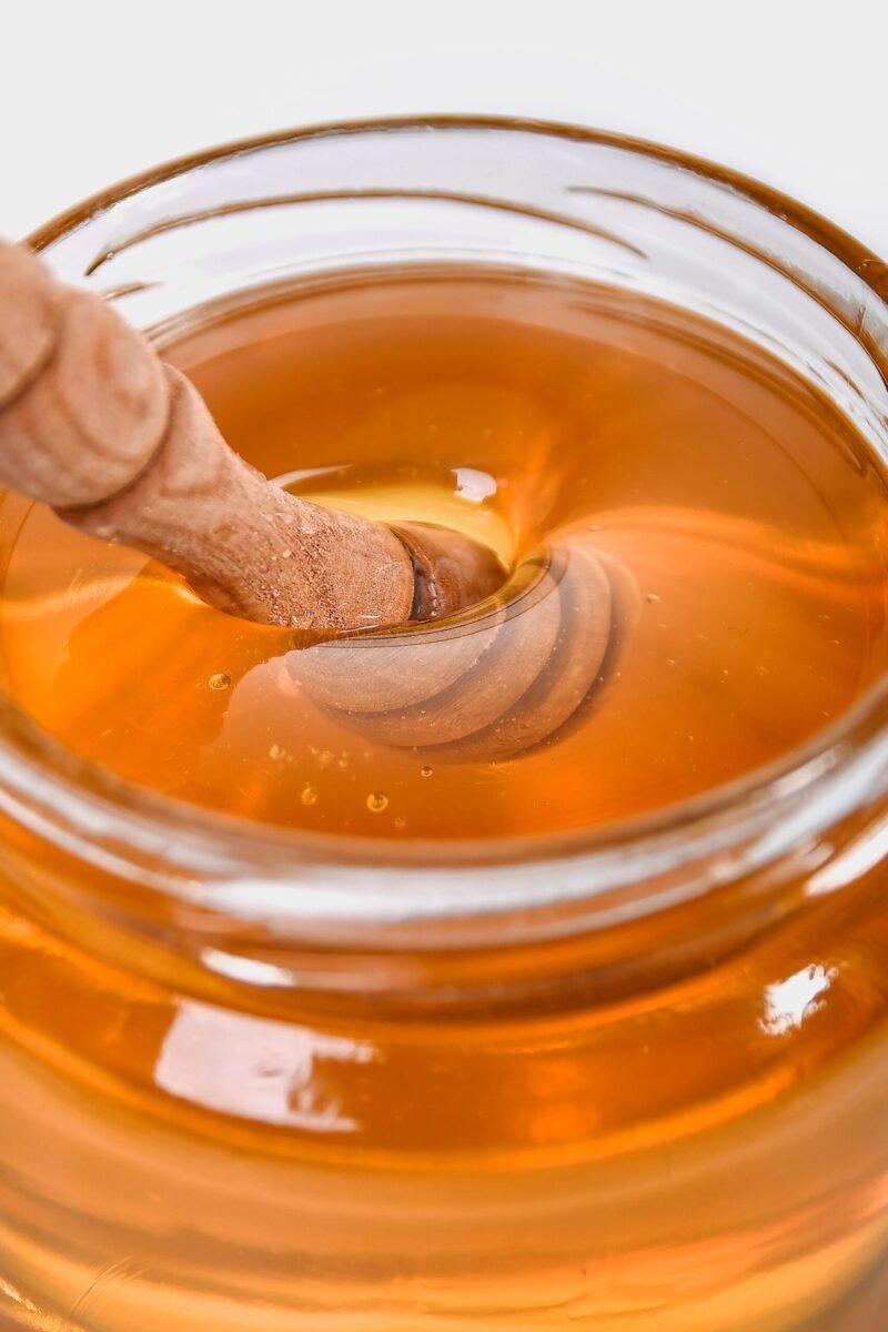 Golden honey drizzling from a wooden dipper in a glass jar, showcasing its rich texture.