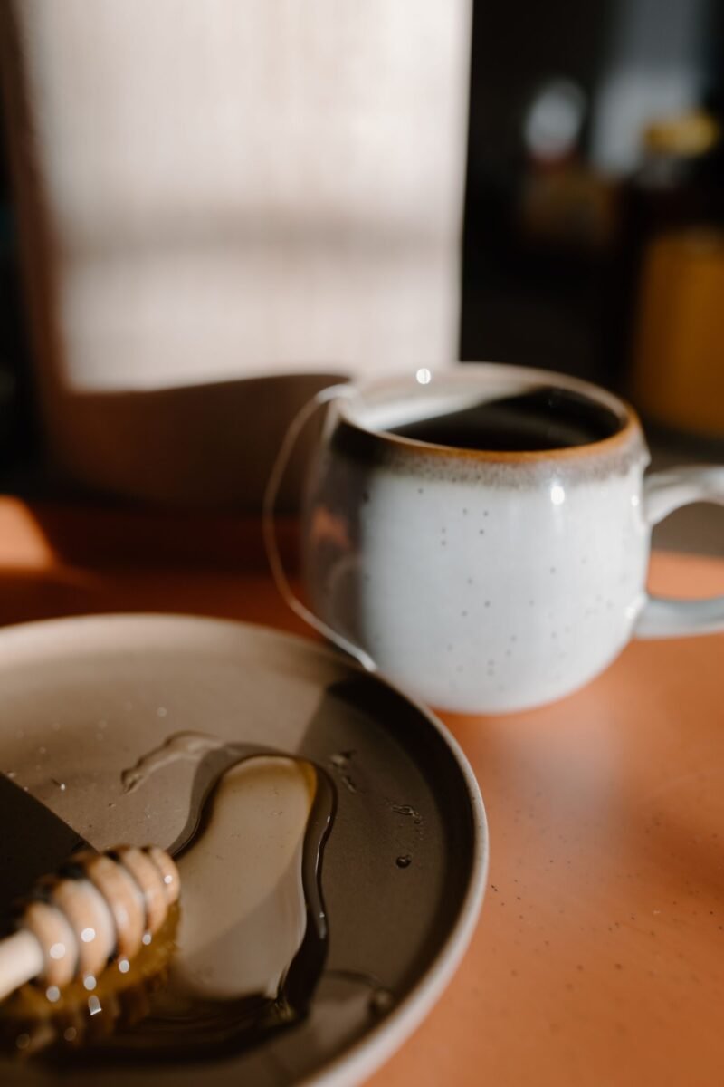 Warm beverage setting with honey dipper and ceramic mug, perfect for a cozy afternoon.